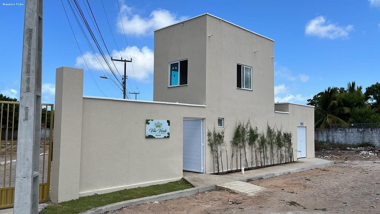 Fachada externa do condomínio com portaria e muro bege.